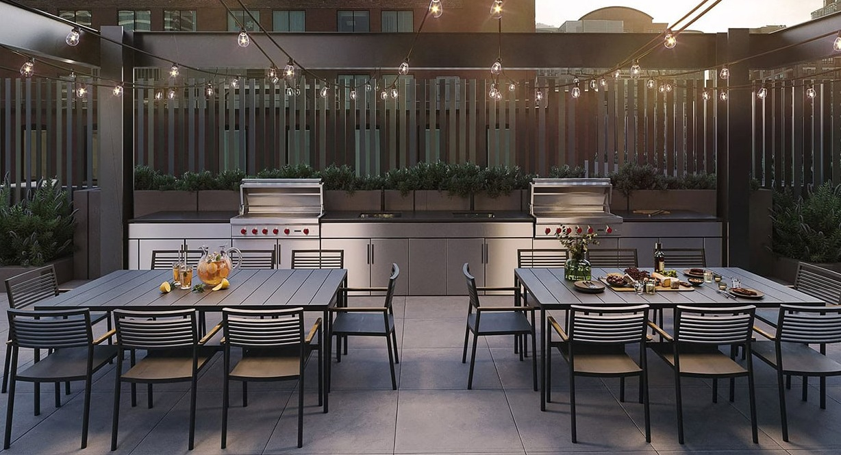 Elegant outdoor dining area with string lights, multiple tables, and modern built-in grills at Hugo Apartments River North in Chicago