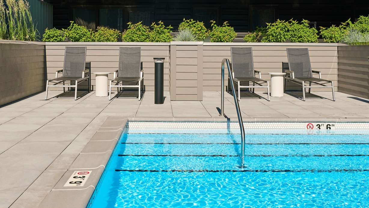 Sparkling outdoor swimming pool with lounge chairs and the apartment building facade in the background at Hugo Apartments River North, Chicago