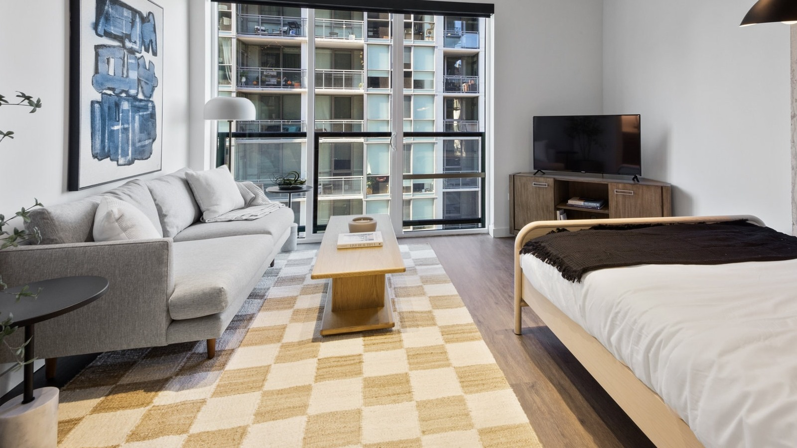 Modern studio apartment combining living and sleeping areas with a sofa, bed, and large windows at Hugo Apartments River North, Chicago