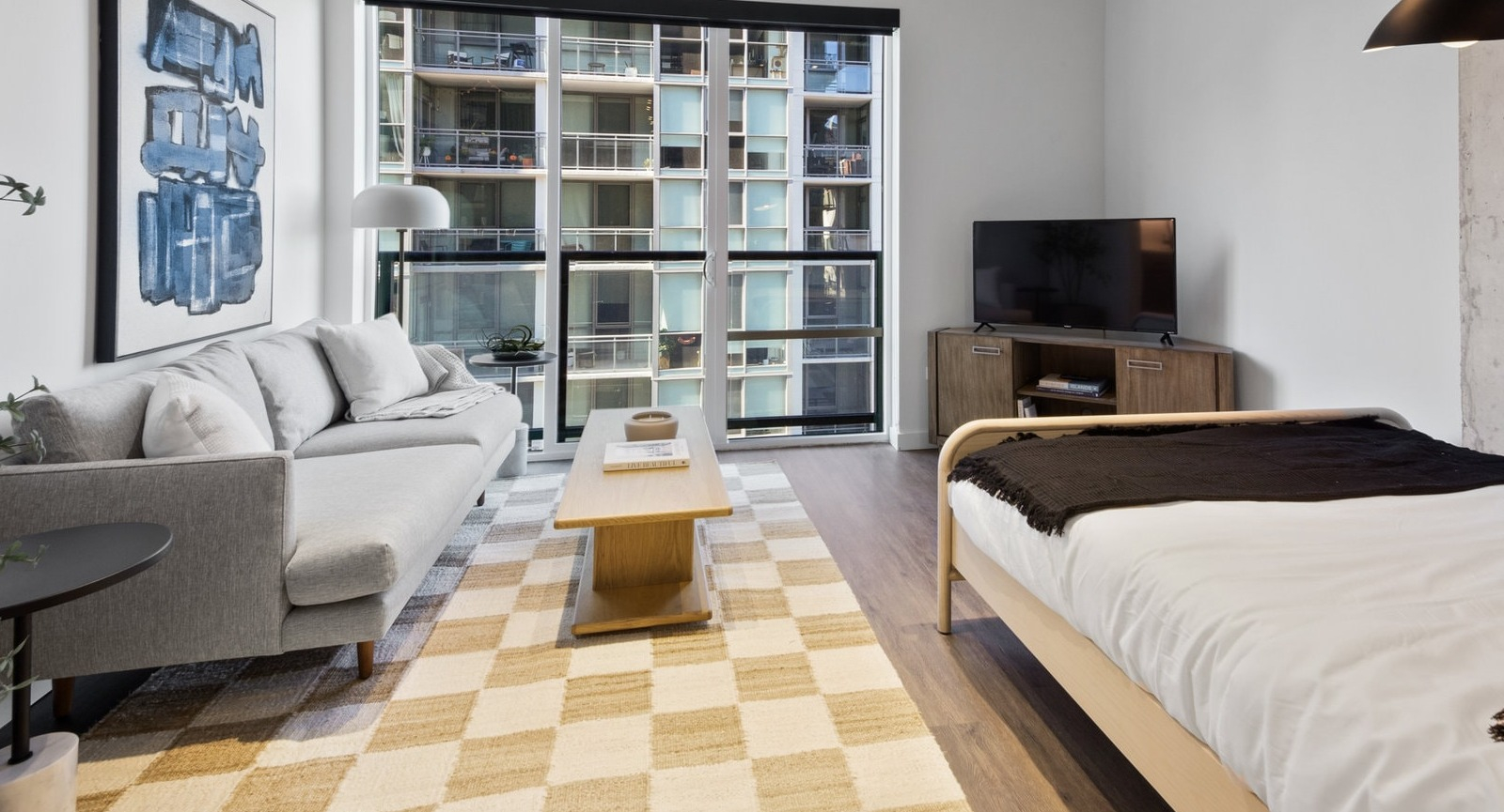 Modern studio apartment combining living and sleeping areas with a sofa, bed, and large windows at Hugo Apartments River North, Chicago