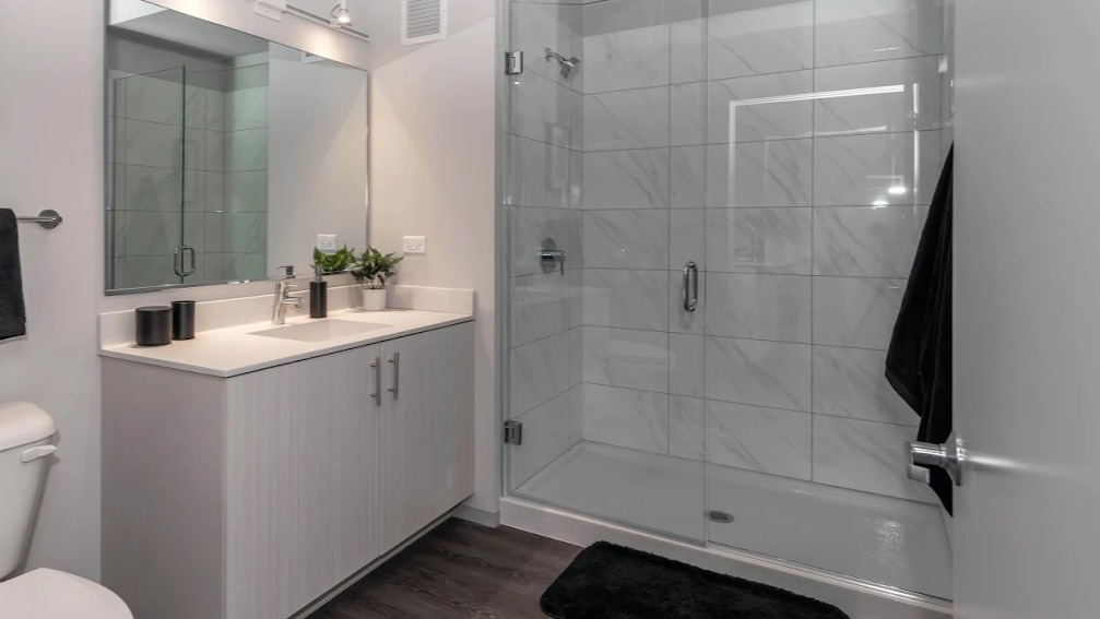 Sleek modern bathroom with a single vanity, large mirror, and a glass-enclosed walk-in shower at Imprint apartments in Chicago