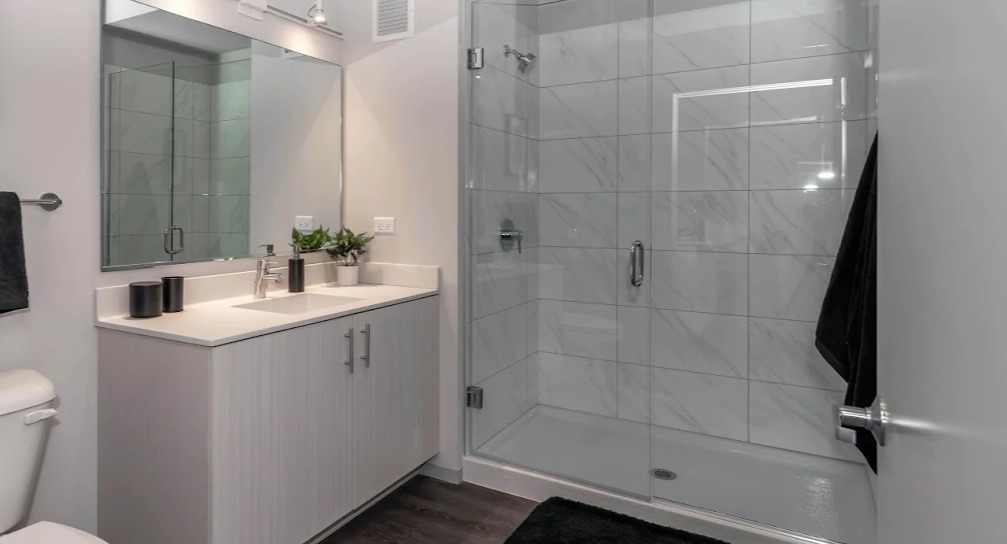 Sleek modern bathroom with a single vanity, large mirror, and a glass-enclosed walk-in shower at Imprint apartments in Chicago