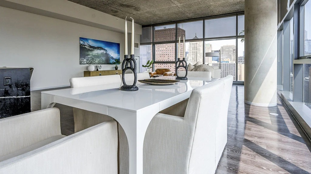 Modern dining room with a white table and chairs, set against a backdrop of large windows offering city views at Imprint apartments in Chicago