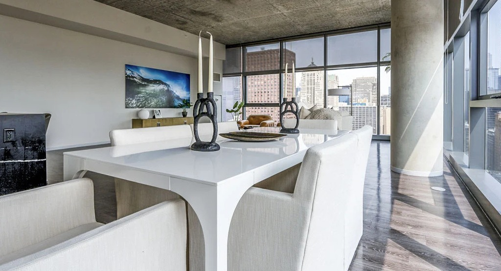Modern dining room with a white table and chairs, set against a backdrop of large windows offering city views at Imprint apartments in Chicago