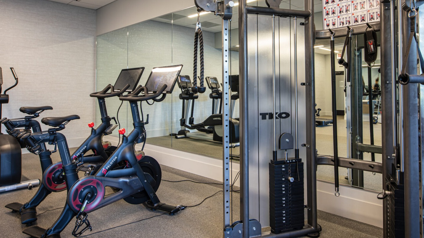 Modern gym with Peloton bikes, weight machines, and a mirrored wall for various workouts at Imprint apartments in Chicago