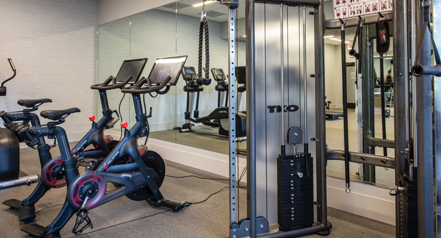 Modern gym with Peloton bikes, weight machines, and a mirrored wall for various workouts at Imprint apartments in Chicago