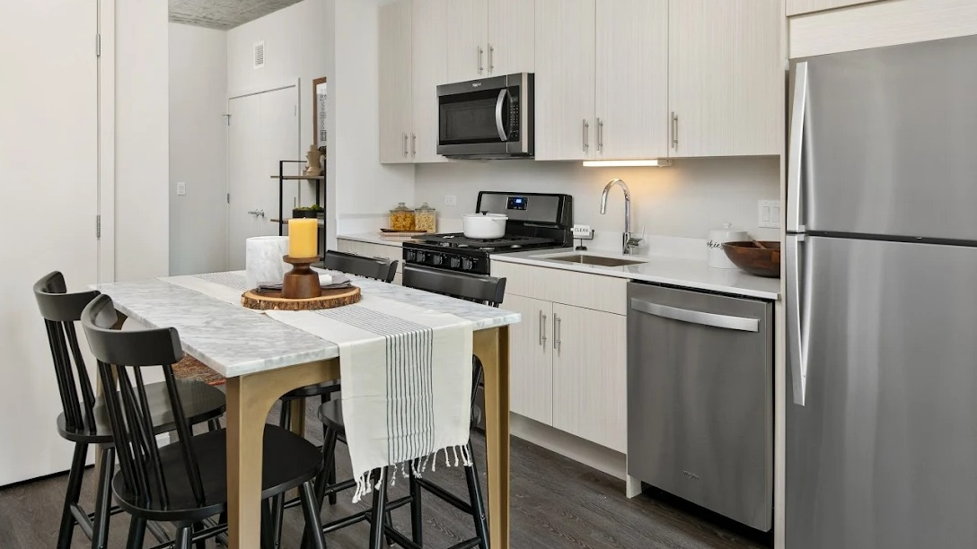 Compact modern kitchen with stainless steel appliances, light cabinetry, and a dining table with chairs at Imprint apartments in Chicago