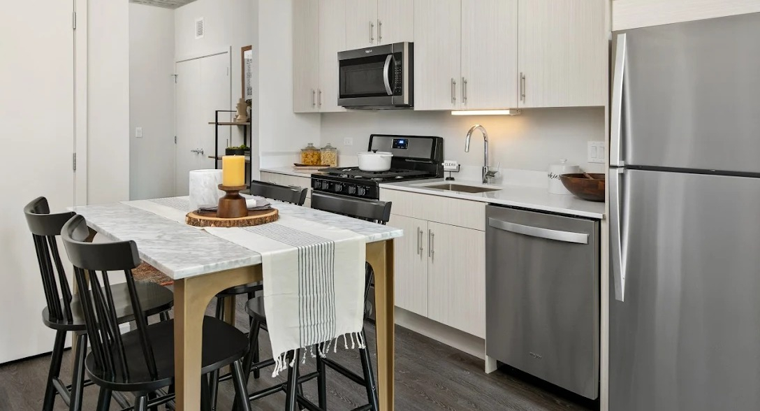 Compact modern kitchen with stainless steel appliances, light cabinetry, and a dining table with chairs at Imprint apartments in Chicago