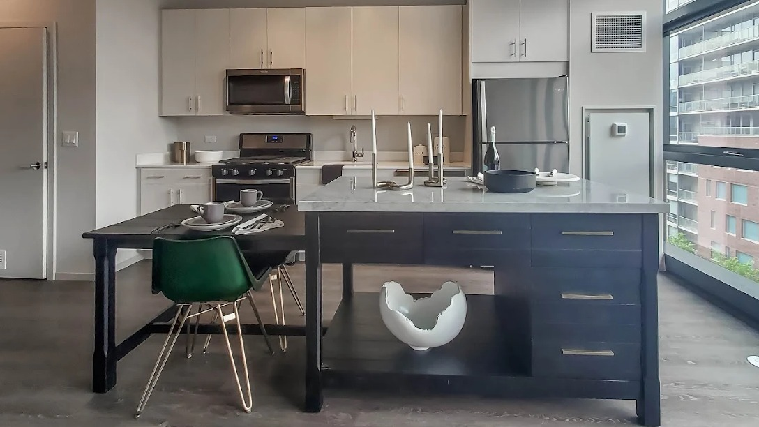 Spacious kitchen with a large dark island, dining table, and light wood cabinetry, illuminated by natural light at Imprint apartments in Chicago