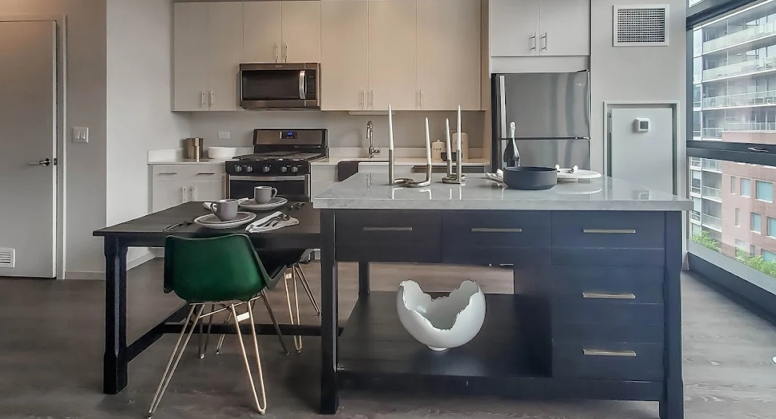 Spacious kitchen with a large dark island, dining table, and light wood cabinetry, illuminated by natural light at Imprint apartments in Chicago