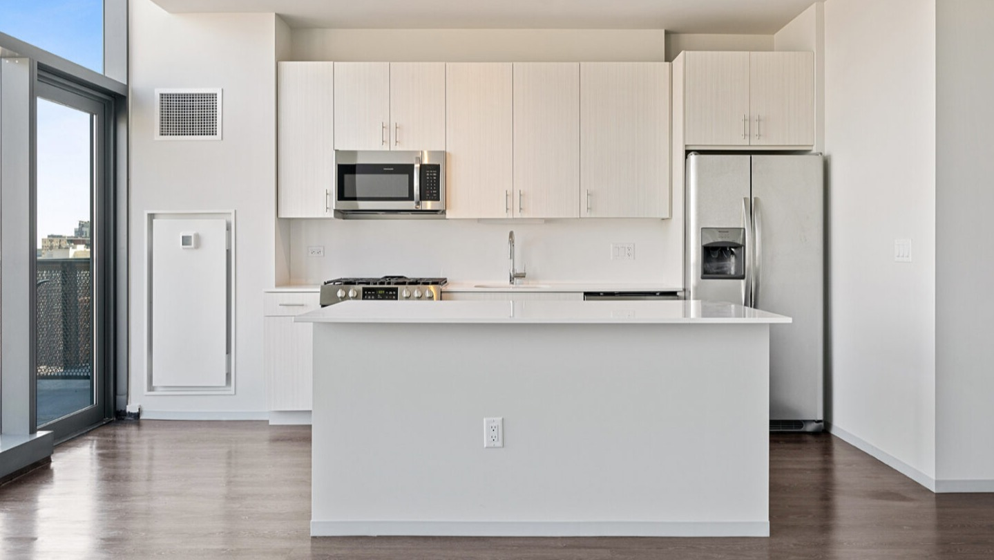 Modern kitchen with a large white island, light cabinetry, stainless steel appliances, and access to a balcony at Imprint apartments in Chicago
