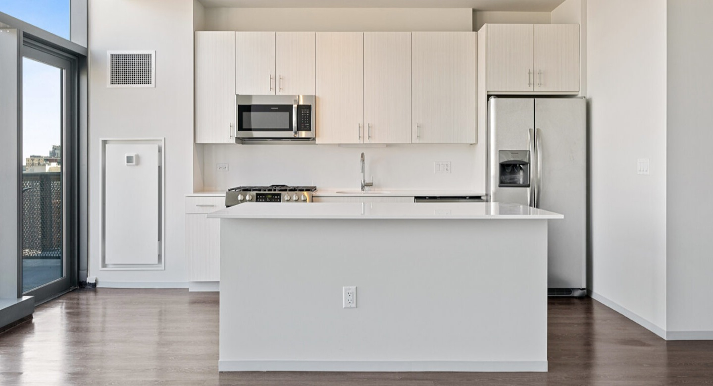 Modern kitchen with a large white island, light cabinetry, stainless steel appliances, and access to a balcony at Imprint apartments in Chicago
