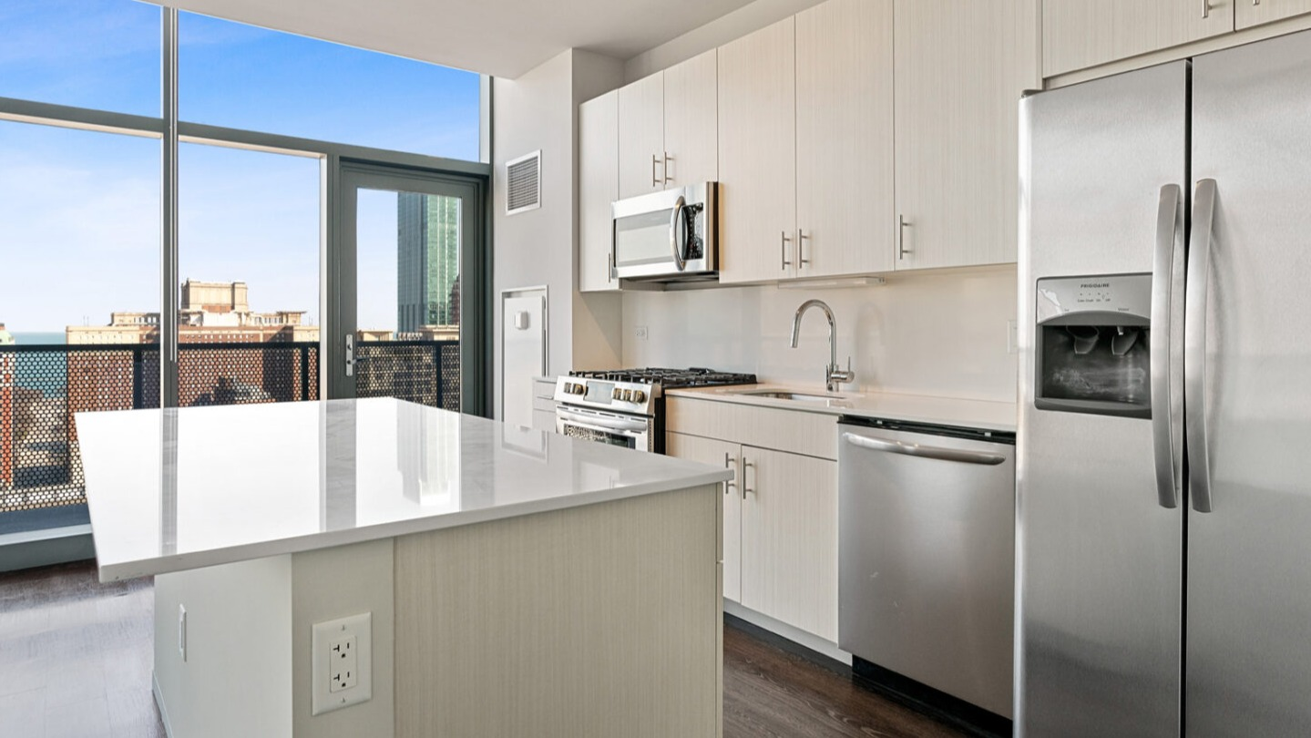 Modern kitchen with a large island, stainless steel appliances, and city views from large windows at Imprint apartments in Chicago
