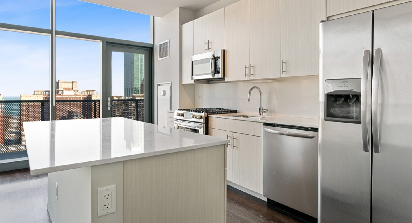 Modern kitchen with a large island, stainless steel appliances, and city views from large windows at Imprint apartments in Chicago