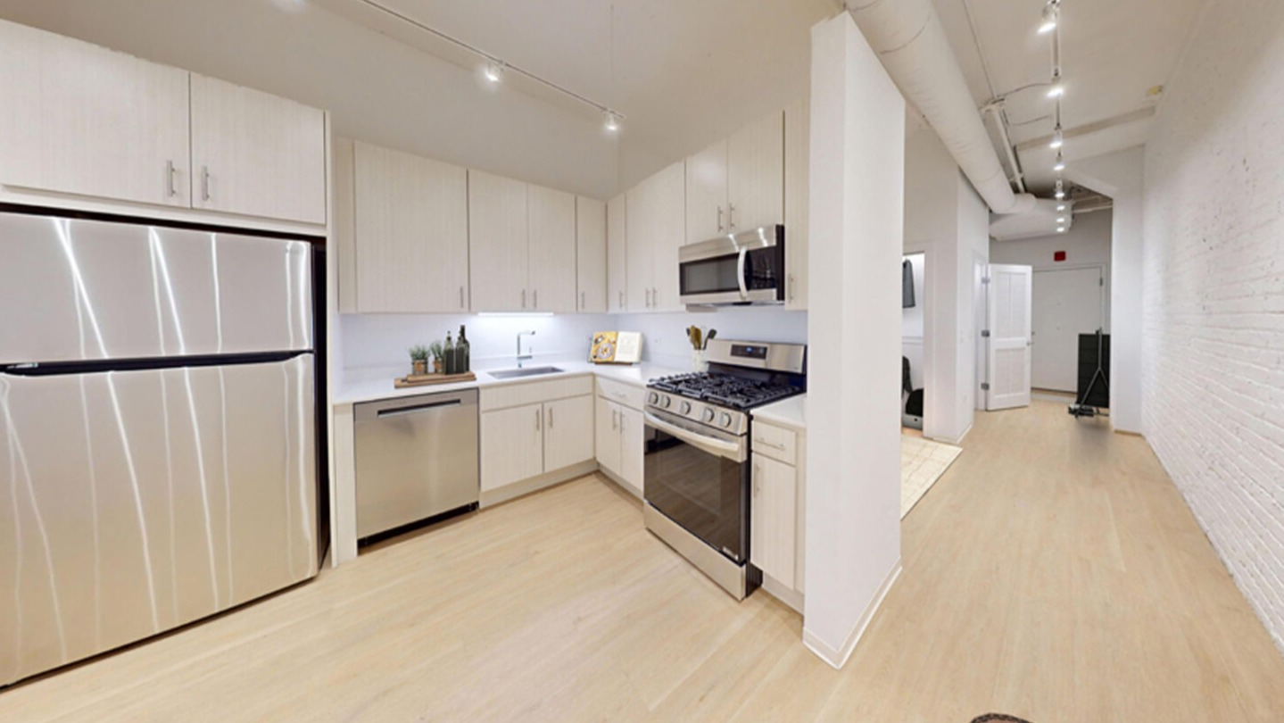 Modern kitchen with light wood cabinetry, white countertops, and stainless steel appliances, including a refrigerator and oven at Imprint apartments in Chicago