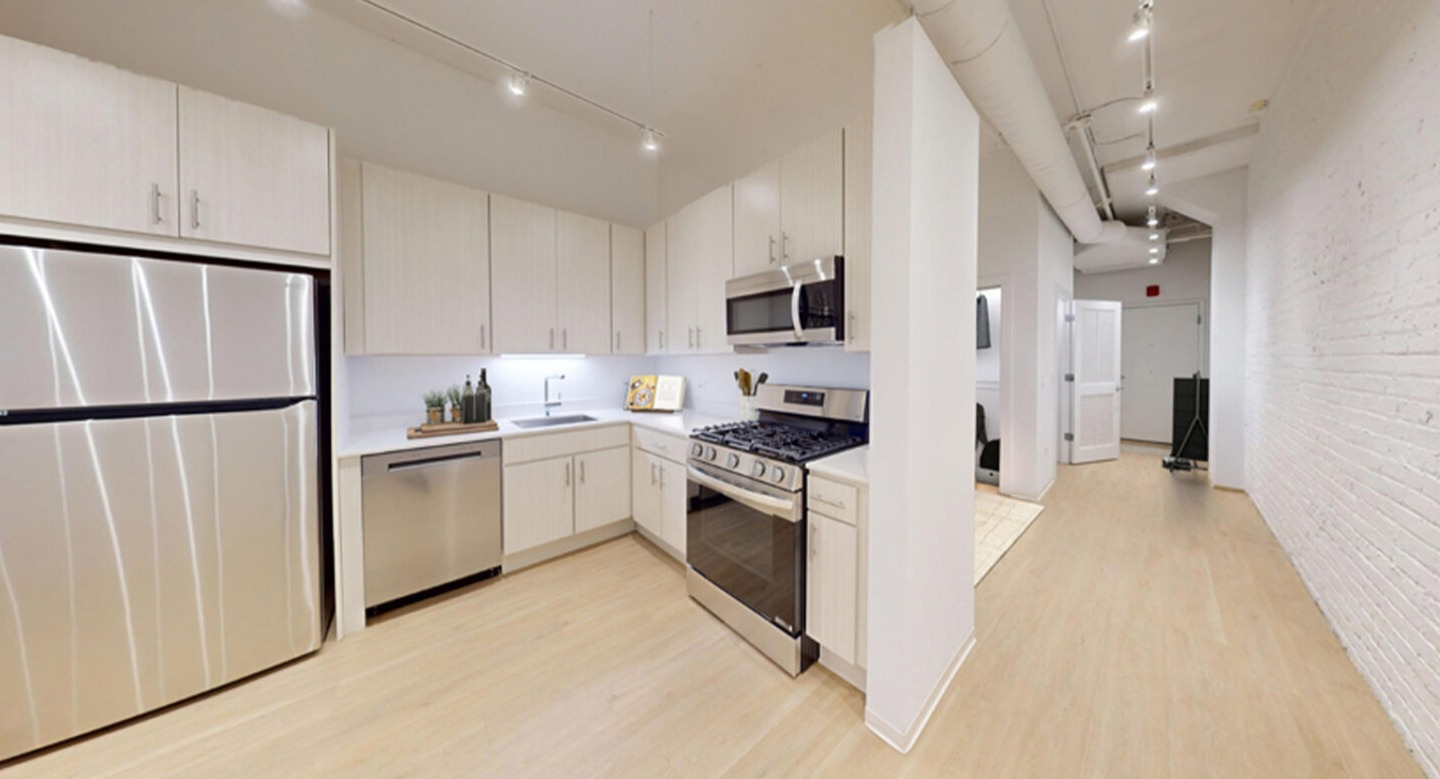 Modern kitchen with light wood cabinetry, white countertops, and stainless steel appliances, including a refrigerator and oven at Imprint apartments in Chicago