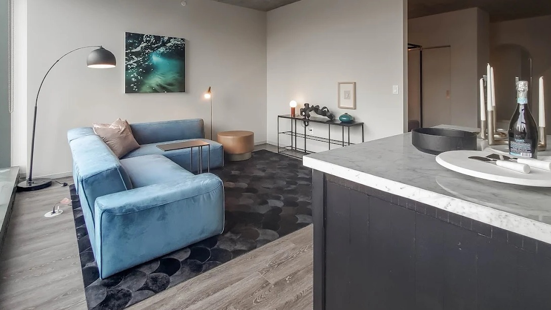 Open concept living room with a blue sectional sofa, modern decor, and a kitchen island visible in the foreground at Imprint apartments in Chicago