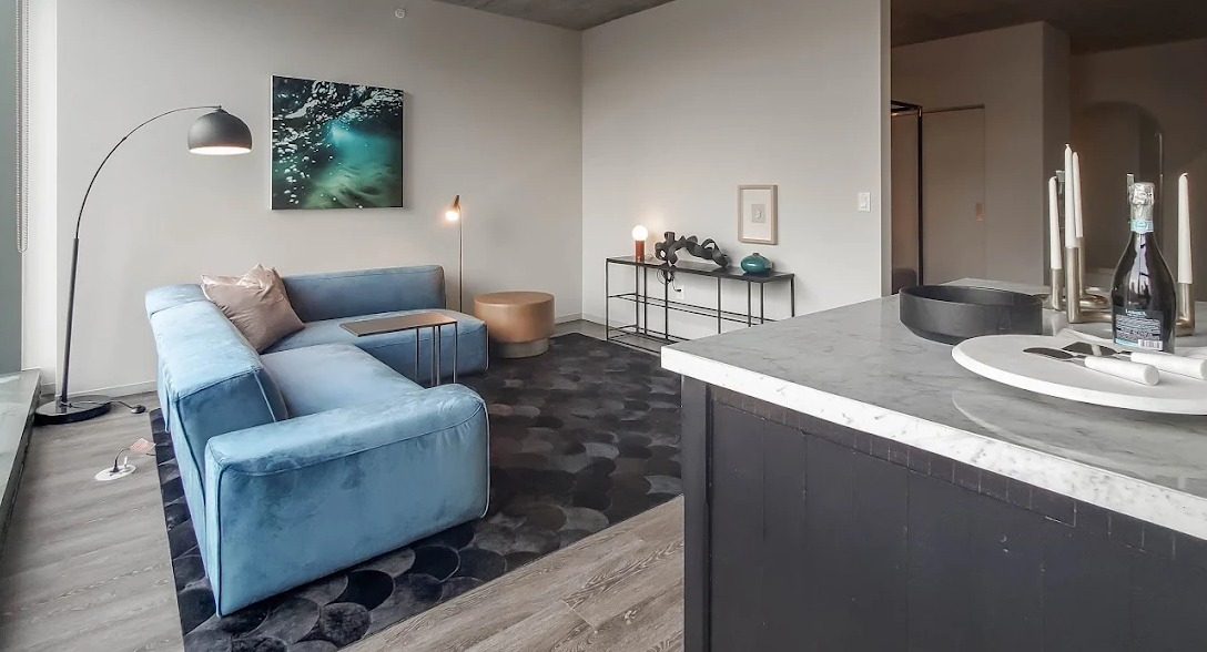 Open concept living room with a blue sectional sofa, modern decor, and a kitchen island visible in the foreground at Imprint apartments in Chicago