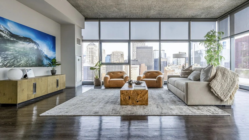 Luxurious living room with a large sofa, leather chairs, and floor-to-ceiling windows offering panoramic city views at Imprint apartments in Chicago