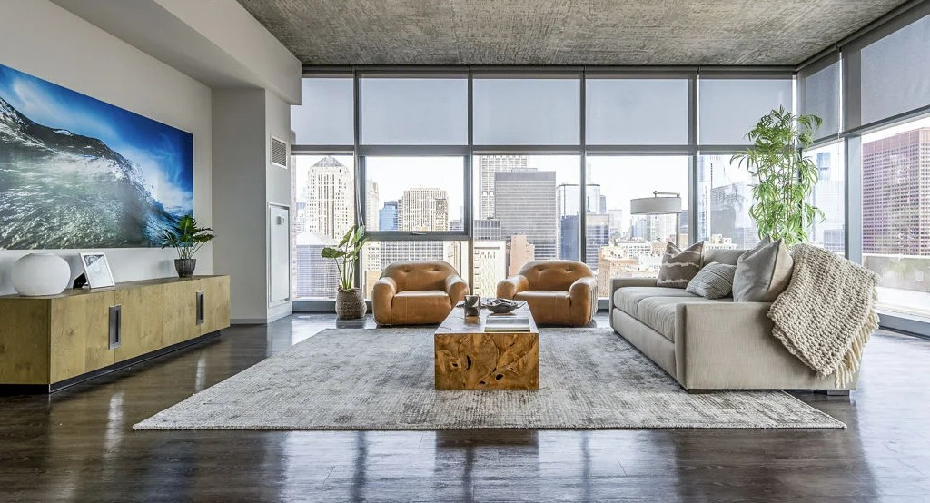 Luxurious living room with a large sofa, leather chairs, and floor-to-ceiling windows offering panoramic city views at Imprint apartments in Chicago