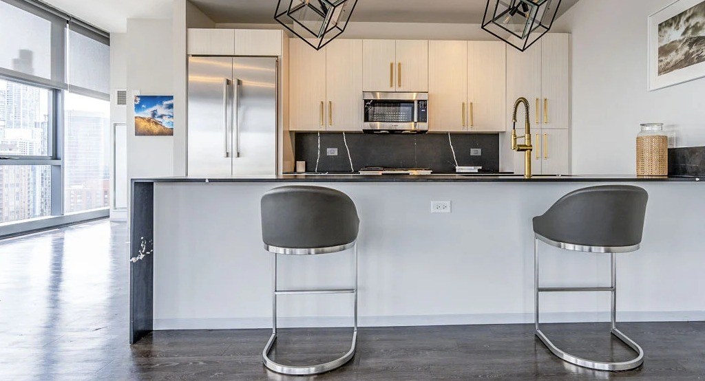 Sleek modern kitchen with light cabinetry, stainless steel appliances, and a breakfast bar with two stools at Imprint apartments in Chicago