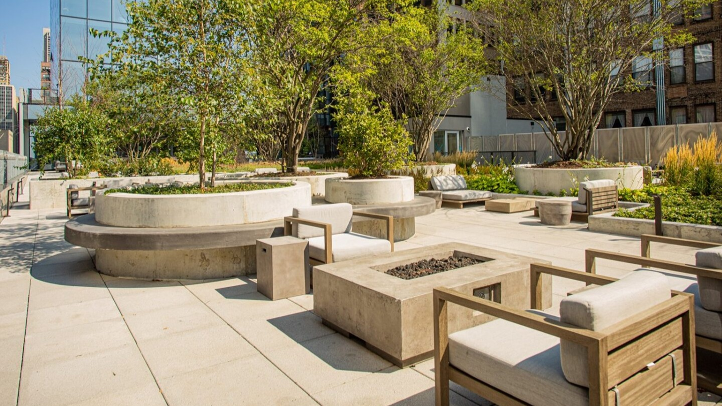 Lush rooftop patio with comfortable outdoor seating, a modern fire pit, and beautiful landscaping at Imprint apartments in Chicago