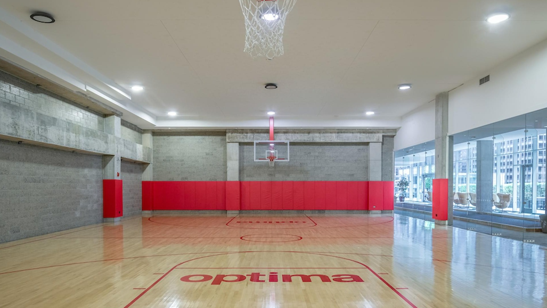 Full-size indoor basketball court with polished wood floors and red accents at Optima Signature apartments in Chicago