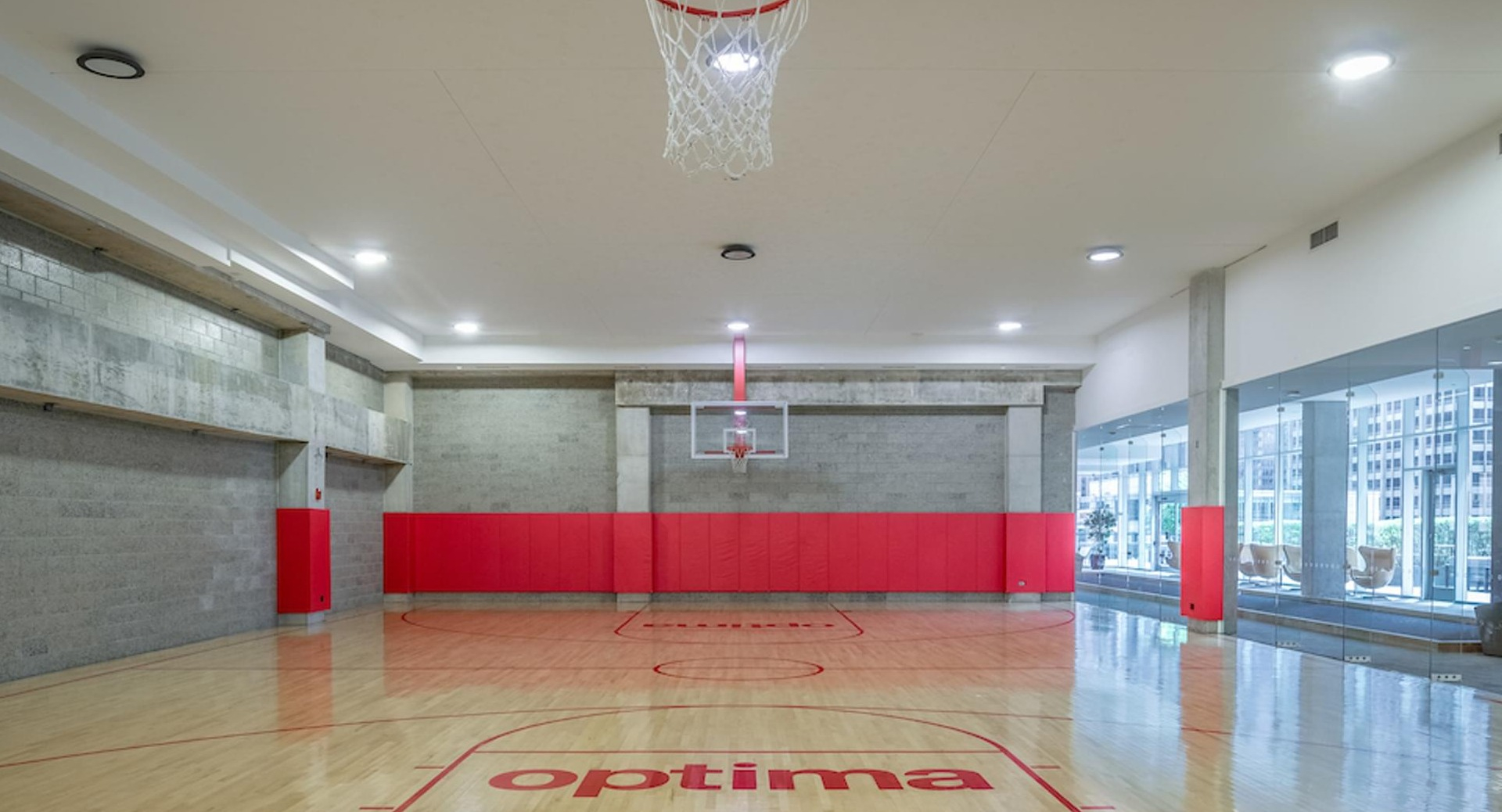 Full-size indoor basketball court with polished wood floors and red accents at Optima Signature apartments in Chicago