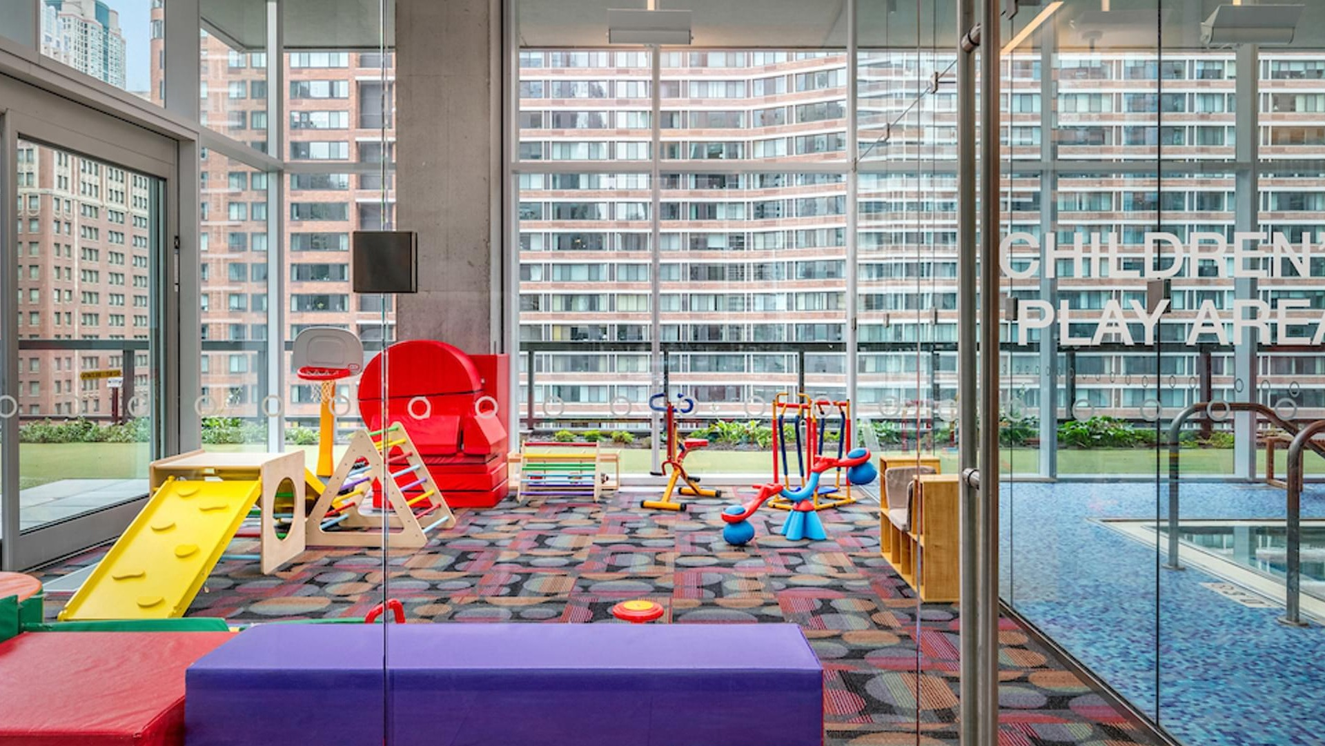 Indoor children’s play area with colorful mats, climbing toys, and large windows at Optima Signature apartments in Chicago