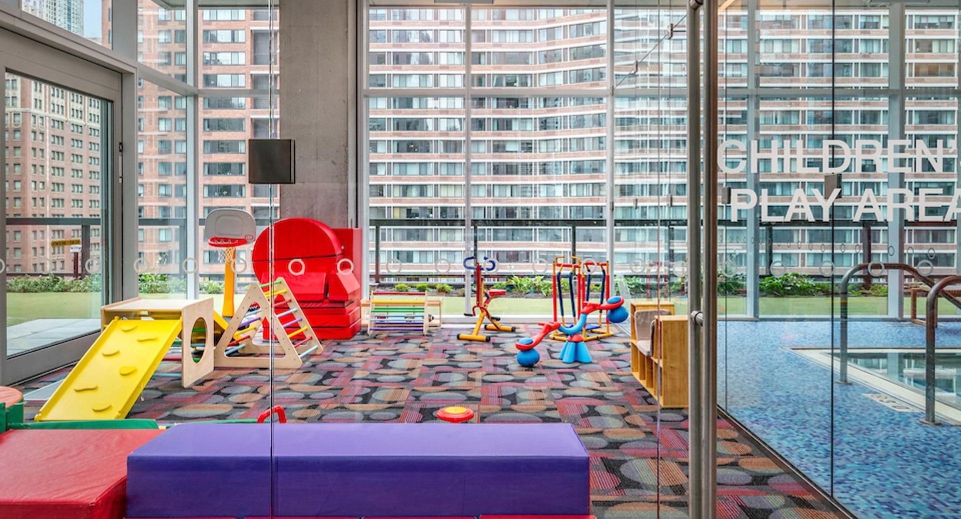 Indoor children’s play area with colorful mats, climbing toys, and large windows at Optima Signature apartments in Chicago