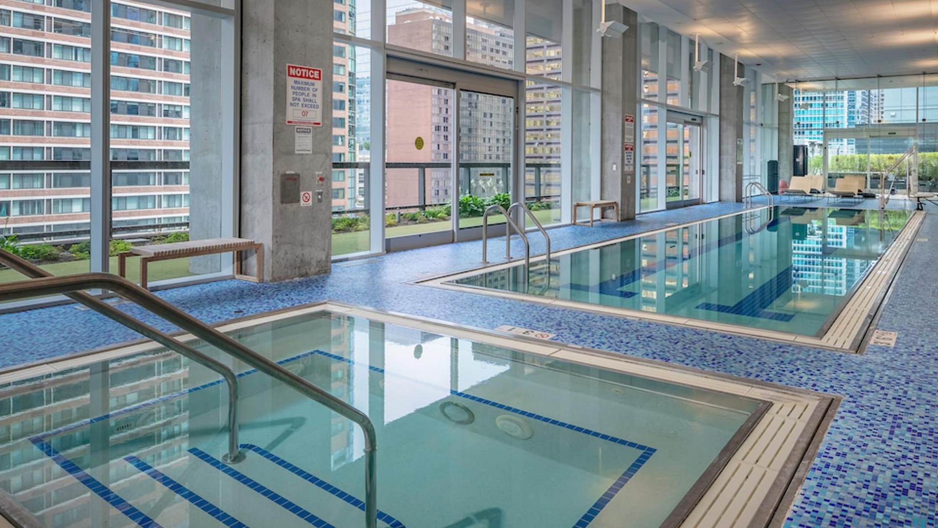 Spacious indoor lap pool and spa with mosaic tile deck and large windows overlooking the city at Optima Signature apartments in Chicago