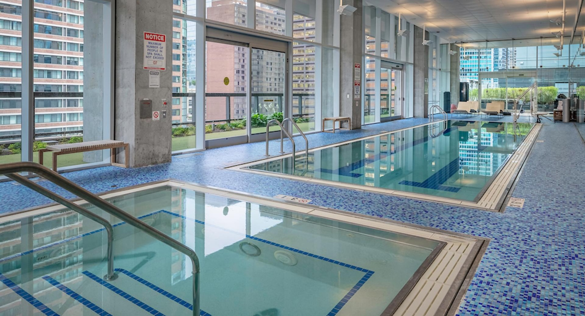 Spacious indoor lap pool and spa with mosaic tile deck and large windows overlooking the city at Optima Signature apartments in Chicago