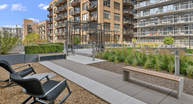 Serene outdoor courtyard featuring various seating options, including benches and lounge chairs, surrounded by greenery at JeffJack Apartments in Chicago