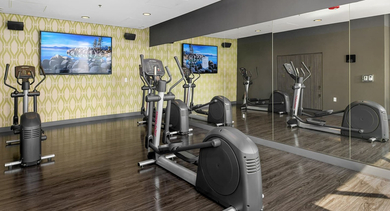 Modern gym area with ellipticals, large mirrors, and TVs for an engaging workout experience at JeffJack Apartments in Chicago