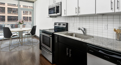 Modern kitchen with granite countertops, stainless steel appliances, and a dining area with balcony access at JeffJack Apartments in Chicago