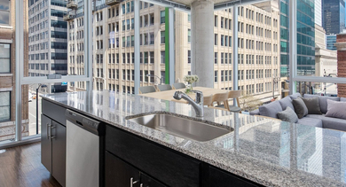 Sleek kitchen island with granite countertops, overlooking the living space and city through floor-to-ceiling windows at JeffJack Apartments in Chicago