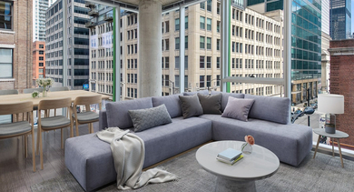 Bright living and dining area with a comfortable sectional, a modern dining table, and stunning corner windows at JeffJack Apartments in Chicago