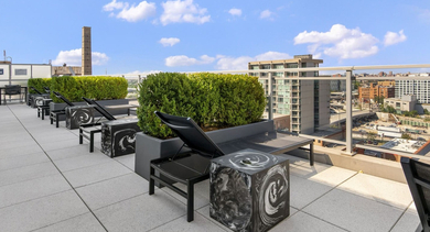 Expansive rooftop sun deck with modern loungers, green planters, and panoramic city views at JeffJack Apartments in Chicago