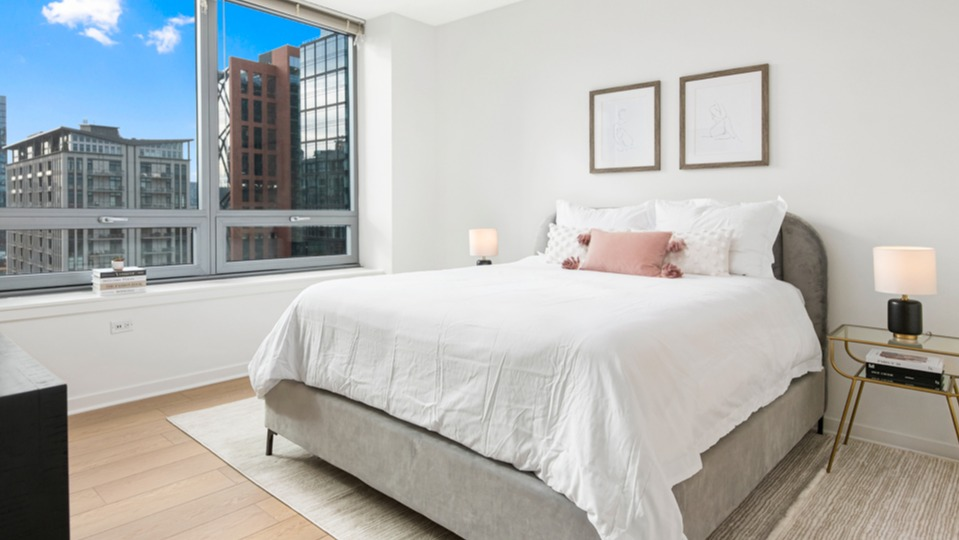Serene apartment bedroom with a comfortable bed, stylish decor, and expansive windows offering captivating city views at K2 Apartments in Chicago