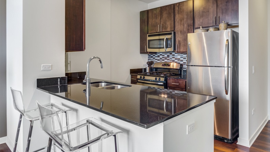 Stylish apartment kitchen featuring a large island with bar seating, stainless steel appliances, and dark wood cabinetry at K2 Apartments in Chicago