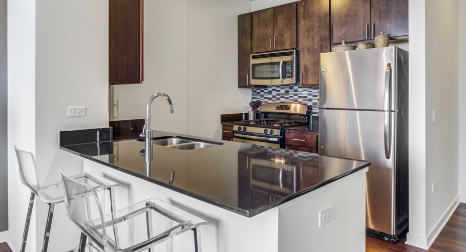 Stylish apartment kitchen featuring a large island with bar seating, stainless steel appliances, and dark wood cabinetry at K2 Apartments in Chicago