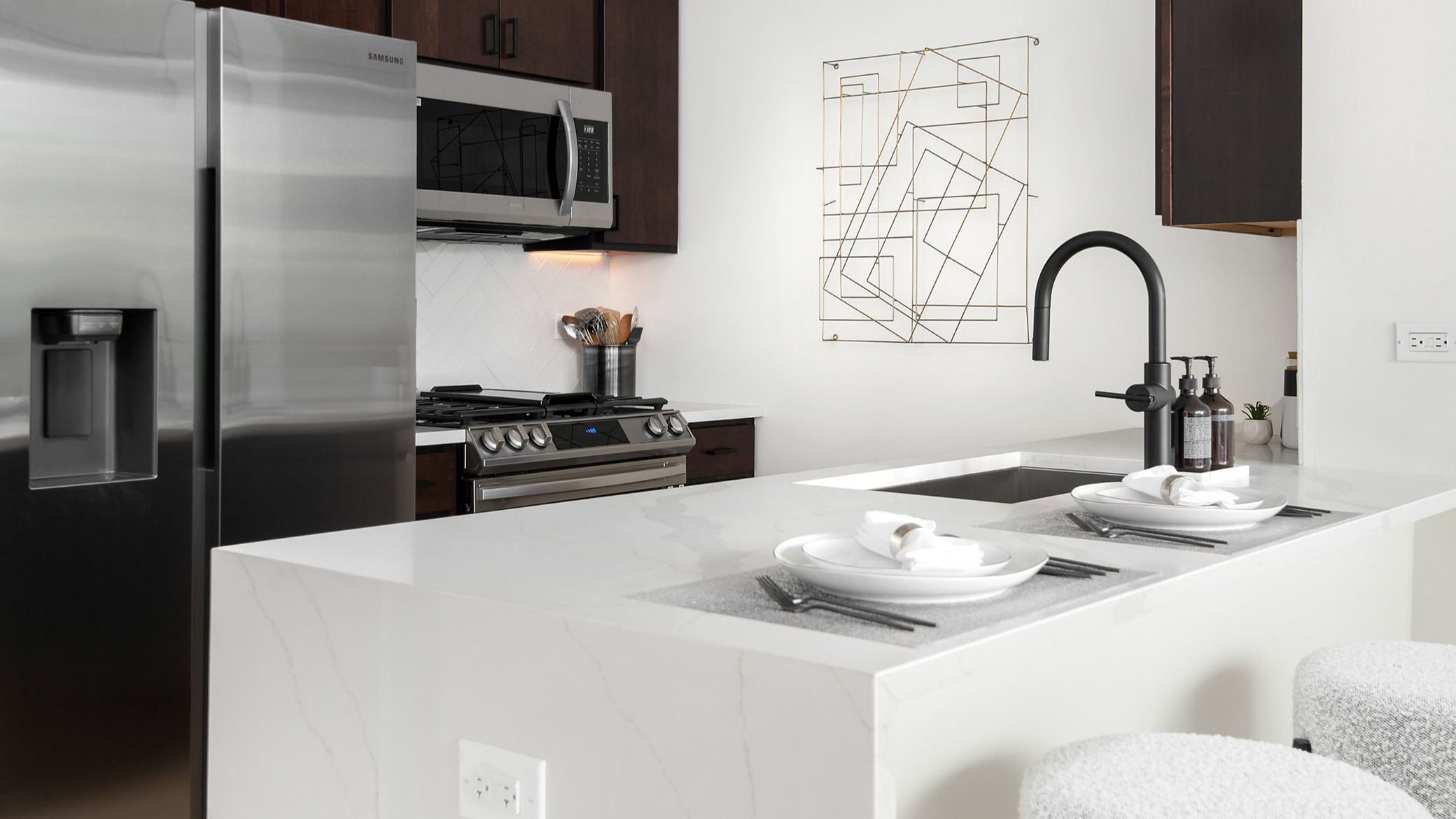 Sleek, modern apartment kitchen featuring a white quartz island with seating, stainless steel appliances, and dark wood cabinetry at K2 Apartments in Chicago