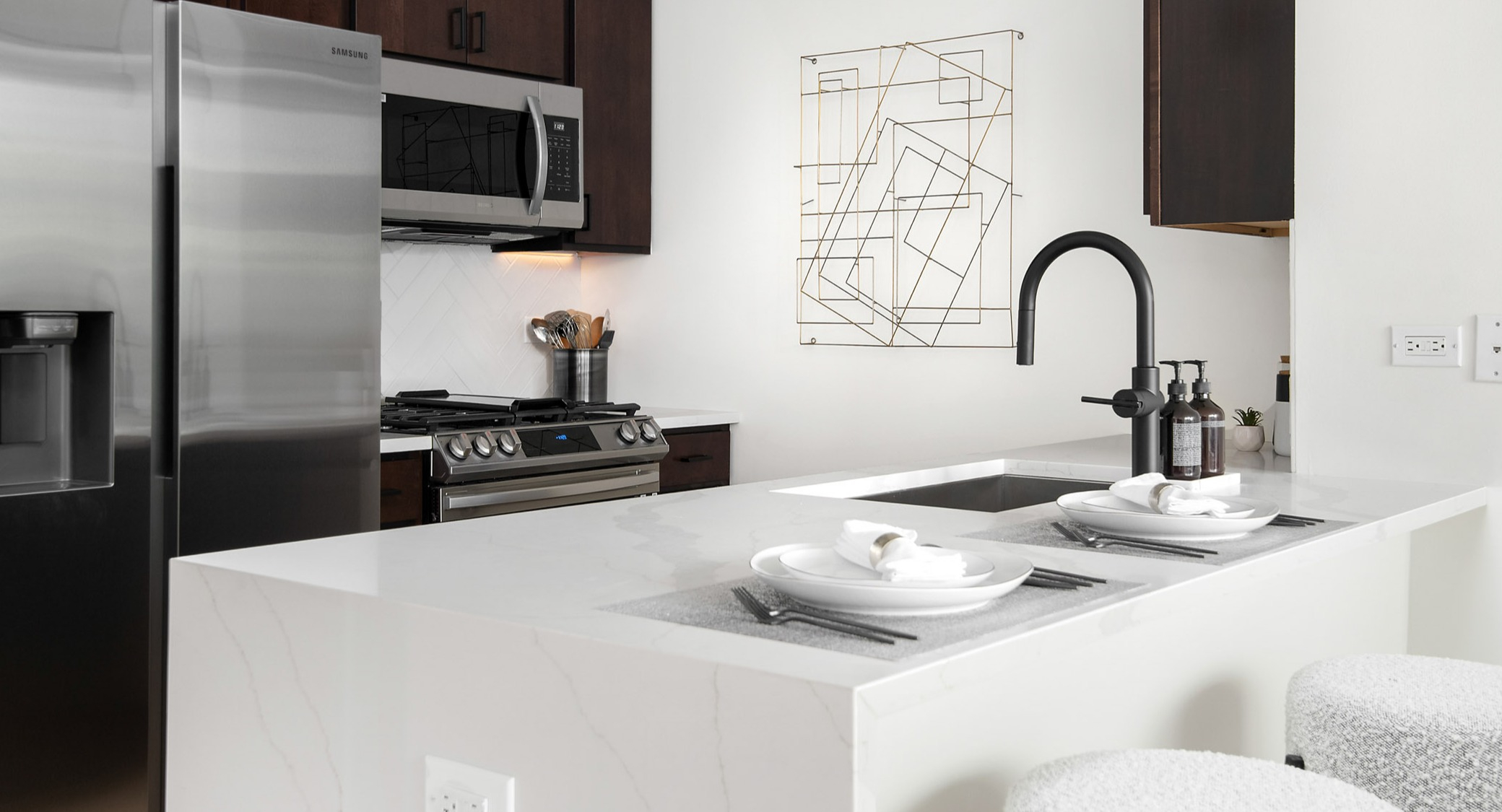 Sleek, modern apartment kitchen featuring a white quartz island with seating, stainless steel appliances, and dark wood cabinetry at K2 Apartments in Chicago
