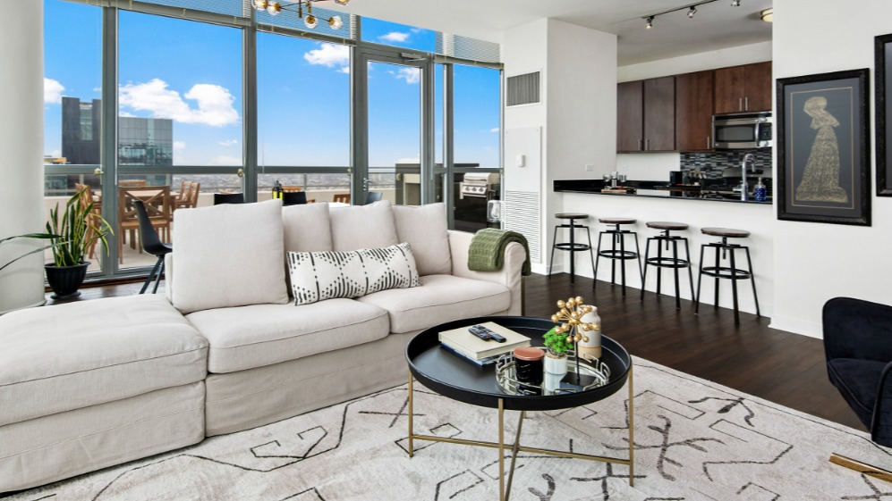 Spacious apartment living room with a large sofa, modern decor, and a balcony offering city views and an outdoor grill at K2 Apartments in Chicago