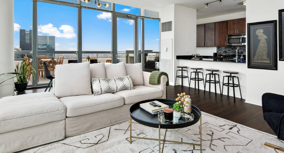 Spacious apartment living room with a large sofa, modern decor, and a balcony offering city views and an outdoor grill at K2 Apartments in Chicago