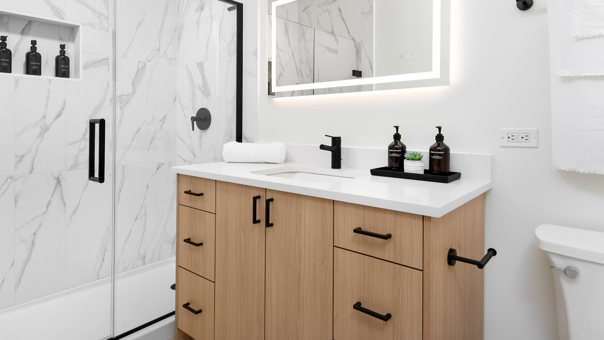 Contemporary bathroom featuring a large vanity, illuminated mirror, and a sleek walk-in shower with marble-look tiles at K2 Apartments in Chicago