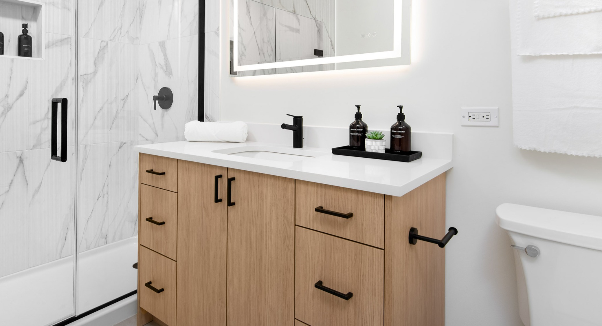 Contemporary bathroom featuring a large vanity, illuminated mirror, and a sleek walk-in shower with marble-look tiles at K2 Apartments in Chicago