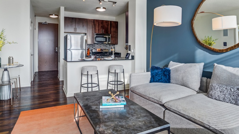 Modern open-concept apartment living room with a comfortable sofa, accent wall, and a view of the adjacent kitchen at K2 Apartments in Chicago