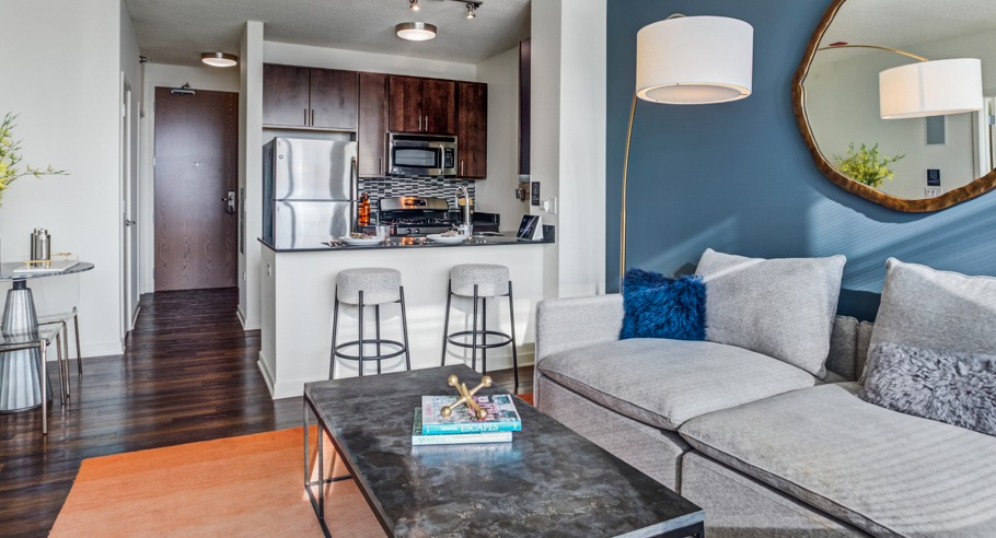Modern open-concept apartment living room with a comfortable sofa, accent wall, and a view of the adjacent kitchen at K2 Apartments in Chicago
