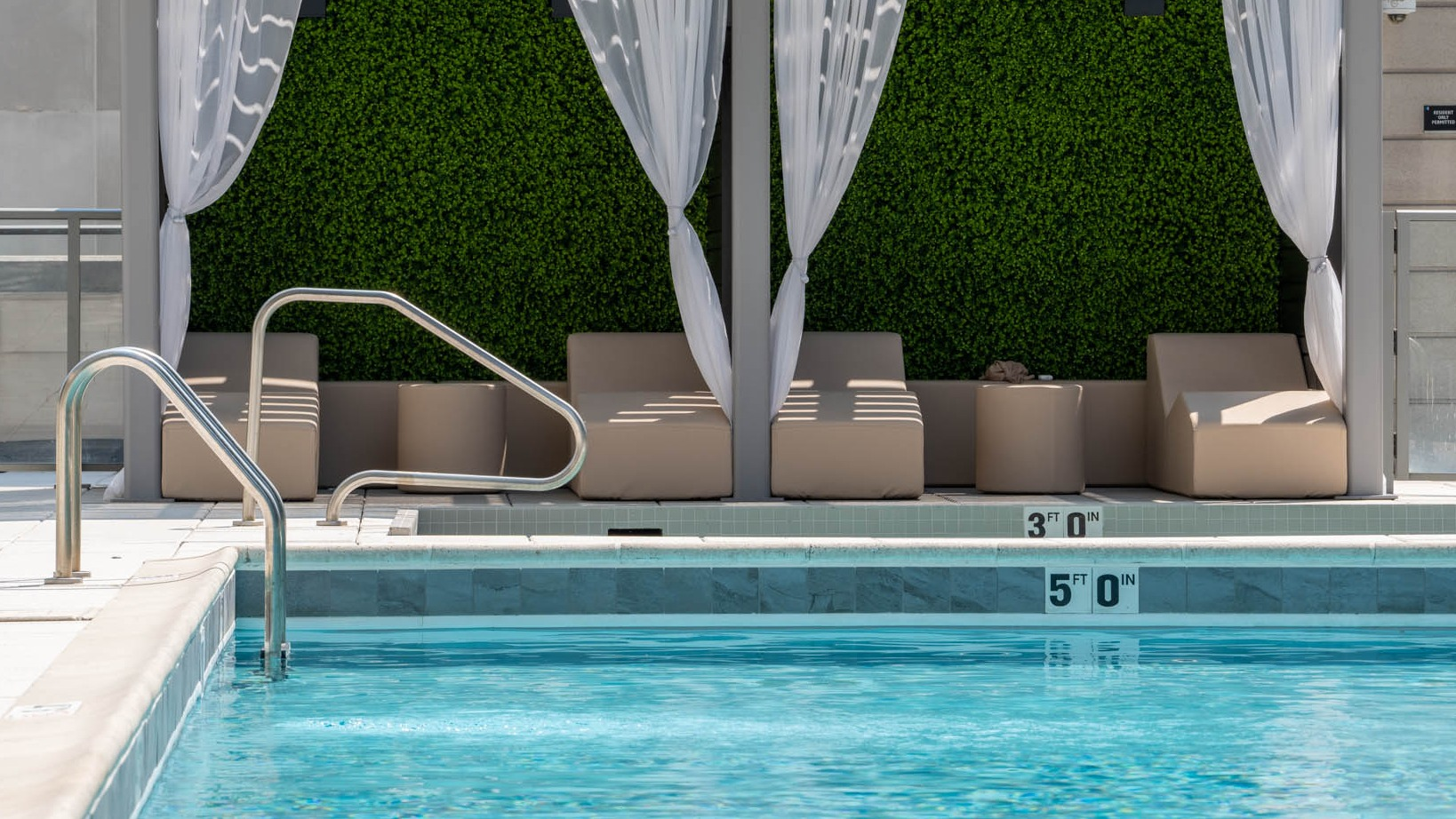 Luxurious poolside area with private cabanas featuring elegant white drapes and lush greenery at K2 Apartments in Chicago